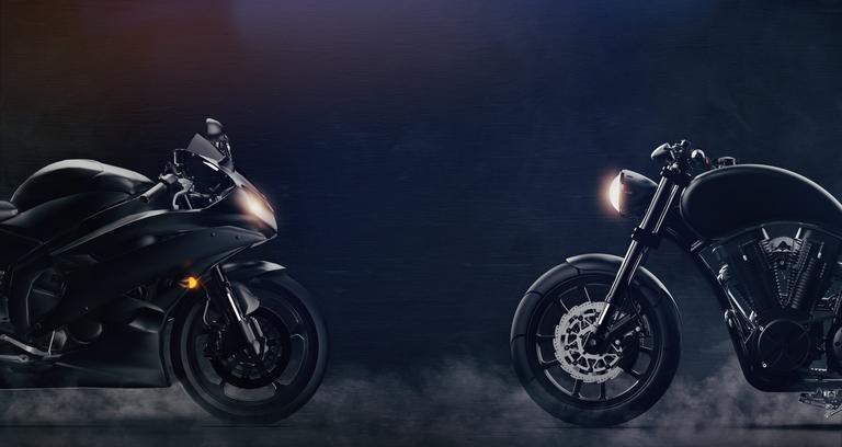 Sportliches und klassisches schwarzes Motorräder stehen sich auf dunklem Untergrund gegenüber.
