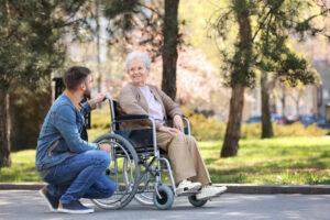 Ältere Frau im Rollstuhl mit jungem Mann im Park