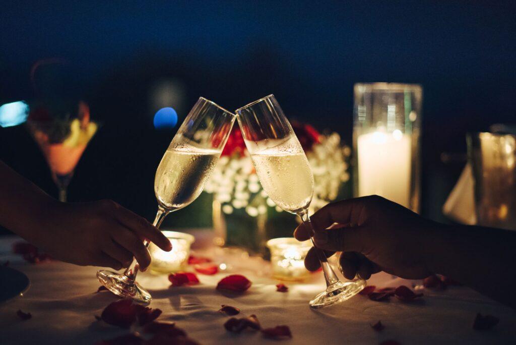 Romantische Kerzenlicht Abendessen Tisch-Setup für Paar mit schönem Licht als Hintergrund. Mann & Frau halten ein Glas Champagner.