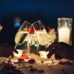 Romantische Kerzenlicht Abendessen Tisch-Setup für Paar mit schönem Licht als Hintergrund. Mann & Frau halten ein Glas Champagner.