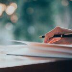 Hand schreibt mit Stift auf Papier bei natürlichem Licht – Lektorat und manuelle Textkorrektur