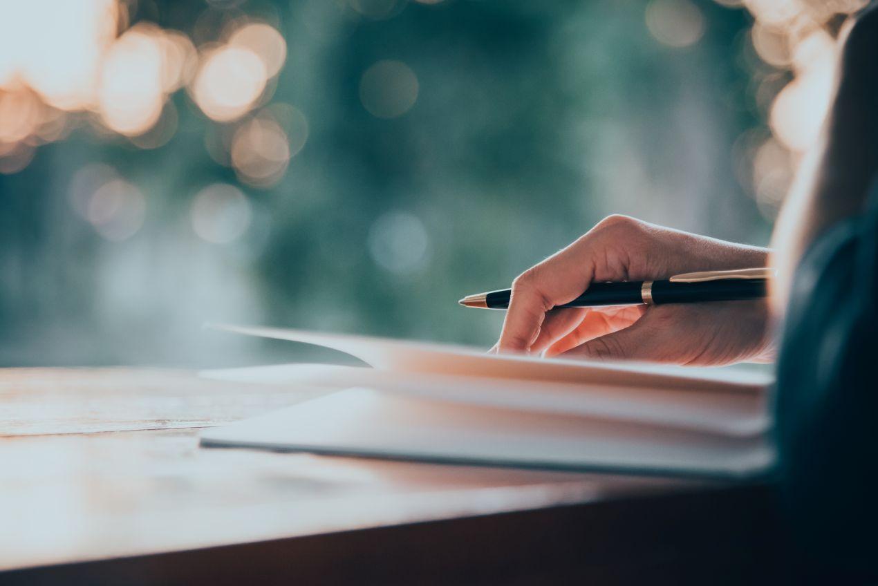 Hand schreibt mit Stift auf Papier bei natürlichem Licht – Lektorat und manuelle Textkorrektur